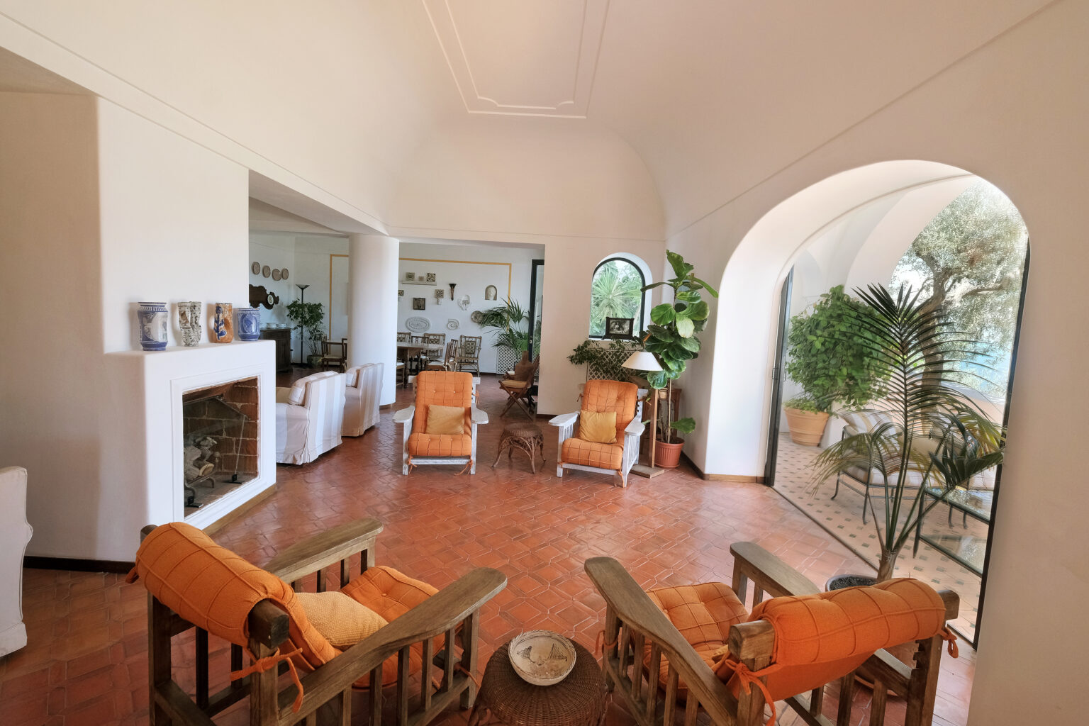 Bright and airy living room featuring orange armchairs, wooden furniture, and large windows with views of greenery, creating a cozy and inviting atmosphere. | Only on SopranoVillas