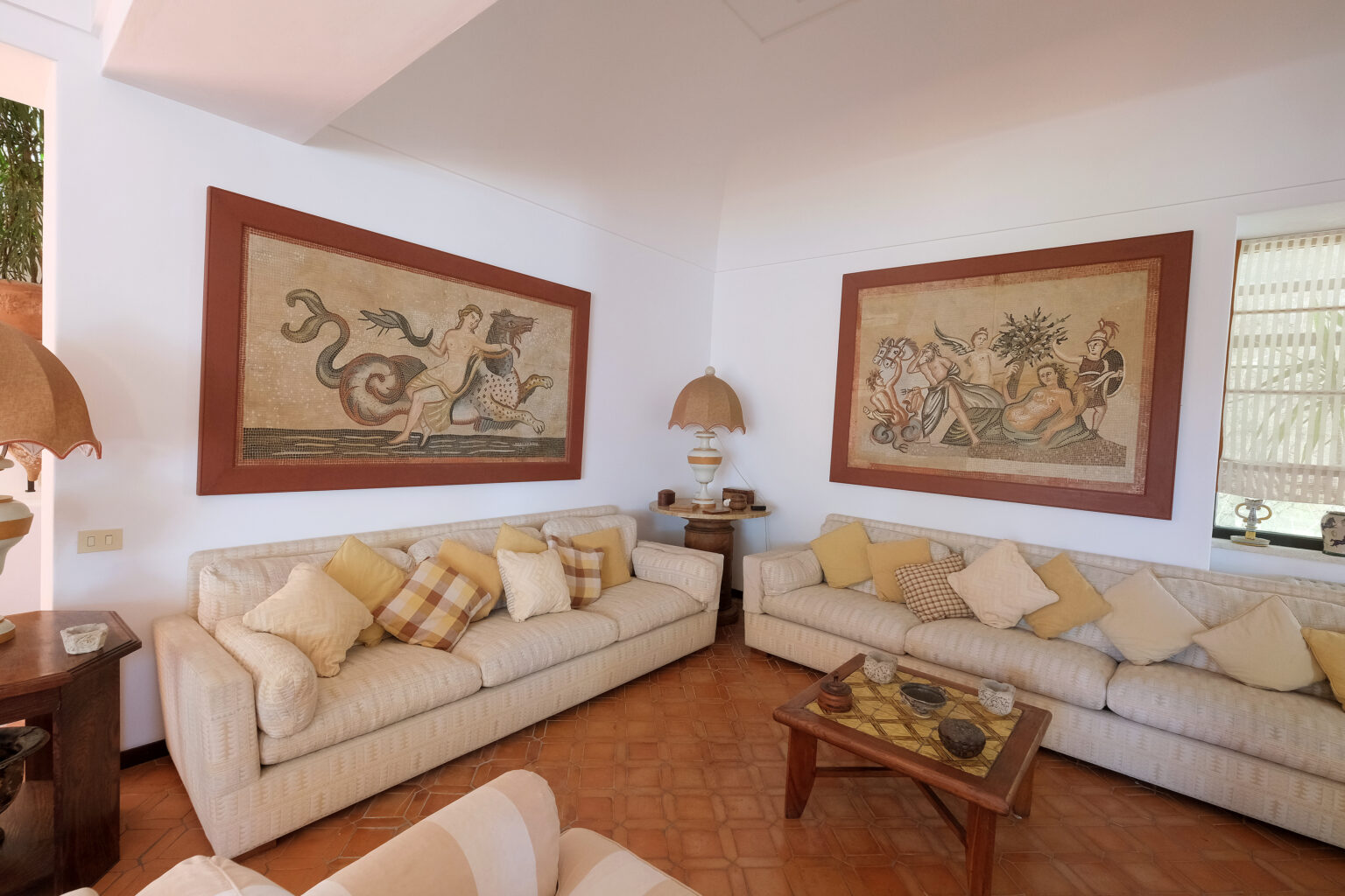 Cozy living room featuring two large wall tapestries, beige sofas adorned with decorative cushions, and a wooden coffee table, creating an inviting atmosphere. | Only on SopranoVillas