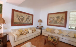 Cozy living room featuring two large wall tapestries, beige sofas adorned with decorative cushions, and a wooden coffee table, creating an inviting atmosphere.