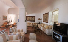 Spacious living room featuring comfortable seating, decorative paintings, and a modern television, with natural light enhancing the warm atmosphere.