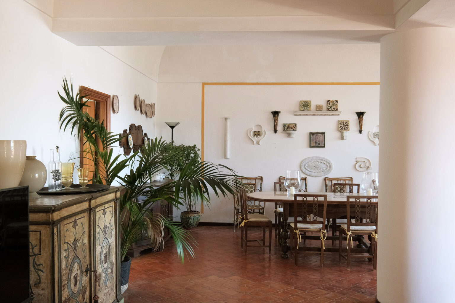 Spacious dining area featuring a wooden table surrounded by chairs, decorated with wall art and plants, showcasing a blend of modern and traditional interior design elements. | Only on SopranoVillas