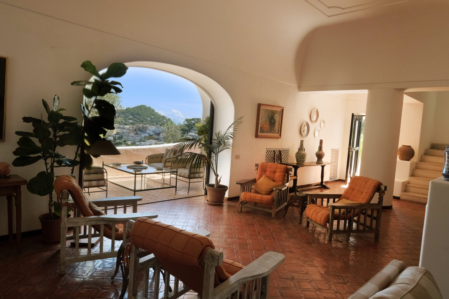 Spacious living room with rustic furniture, large windows showcasing a scenic view, and indoor plants, creating a warm and inviting atmosphere. | Only on SopranoVillas