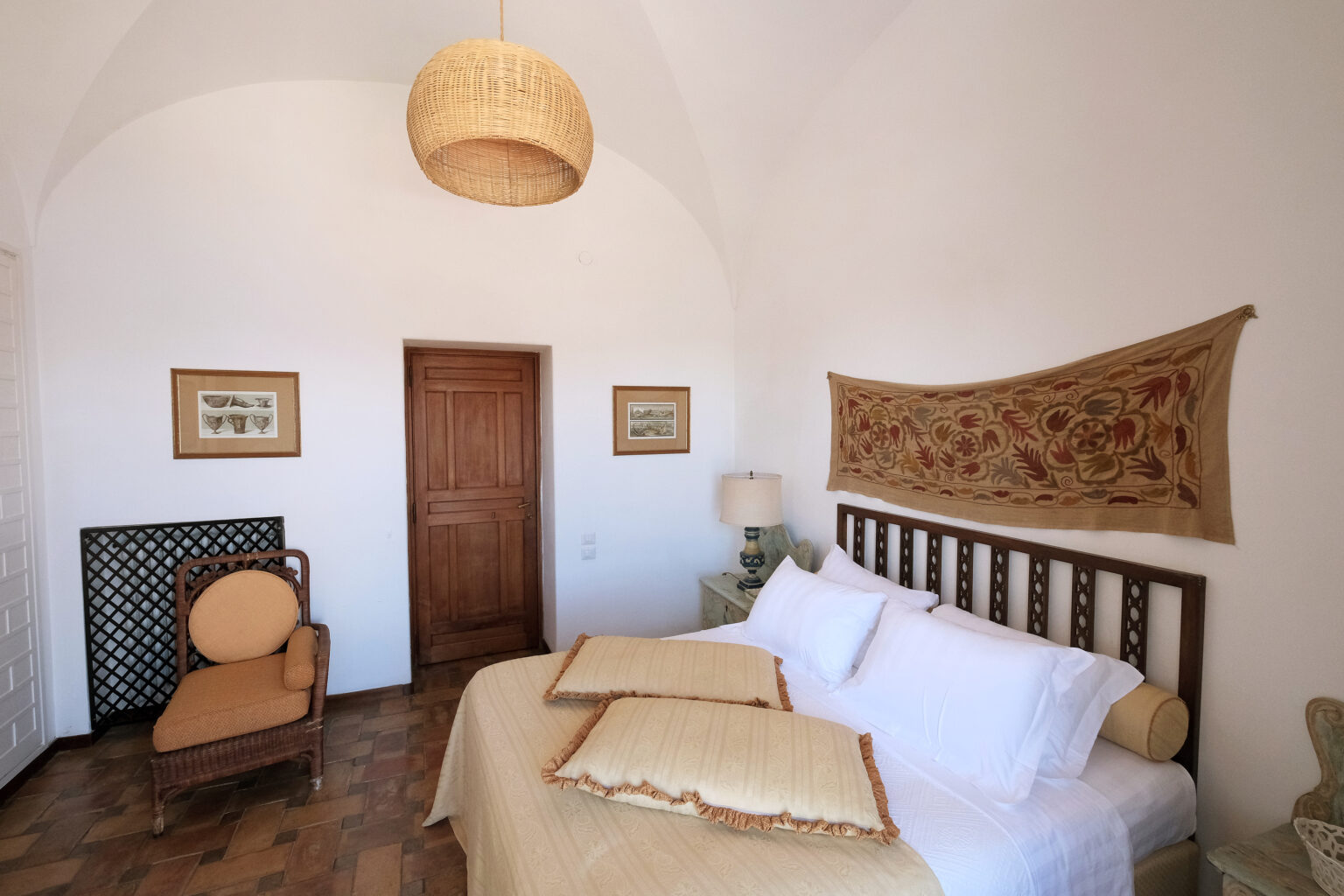 Cozy bedroom featuring a comfortable bed with decorative pillows, a woven wall hanging, a stylish wooden chair, and warm lighting from a pendant lamp, set in a serene and inviting atmosphere. | Only on SopranoVillas