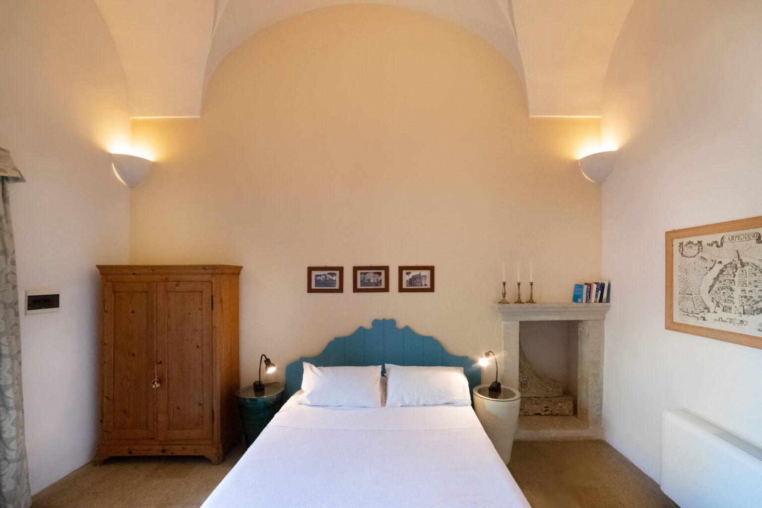 Cozy bedroom interior featuring a double bed with blue headboard, wooden wardrobe, and decorative wall art. The room has soft lighting, a stone fireplace, and a minimalist design, creating a serene atmosphere. Ideal for relaxation and comfort. | Only on SopranoVillas