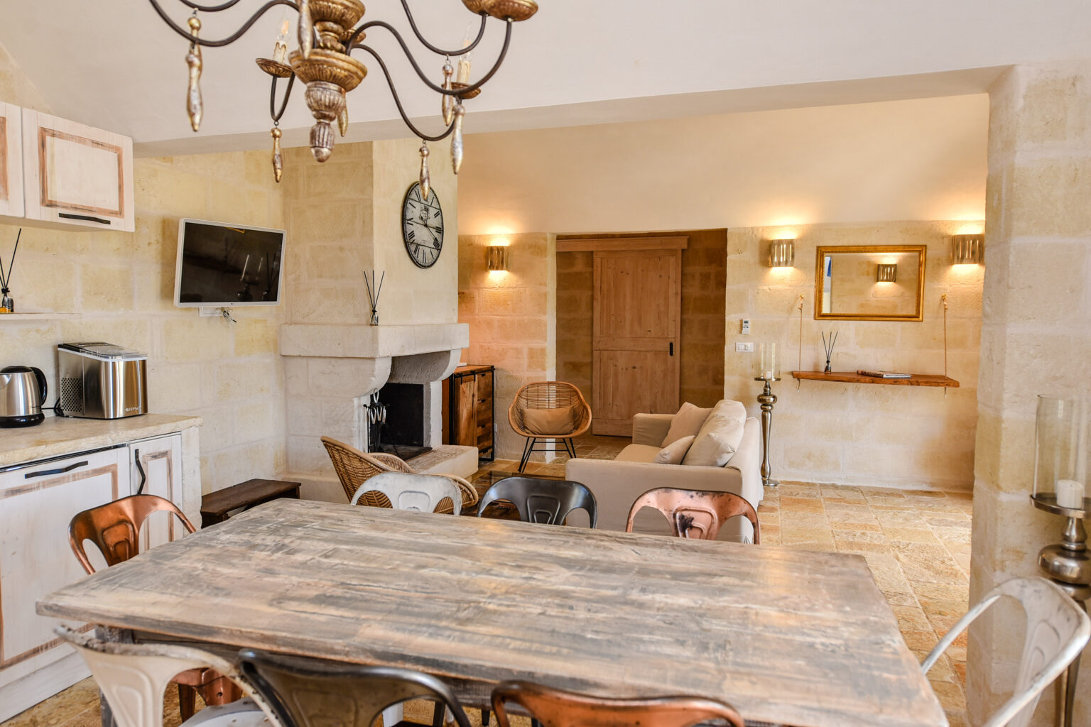 Cozy kitchen and dining area featuring a rustic wooden table, stylish chairs, a modern chandelier, and a stone fireplace, with a view of a comfortable living space. | Only on SopranoVillas