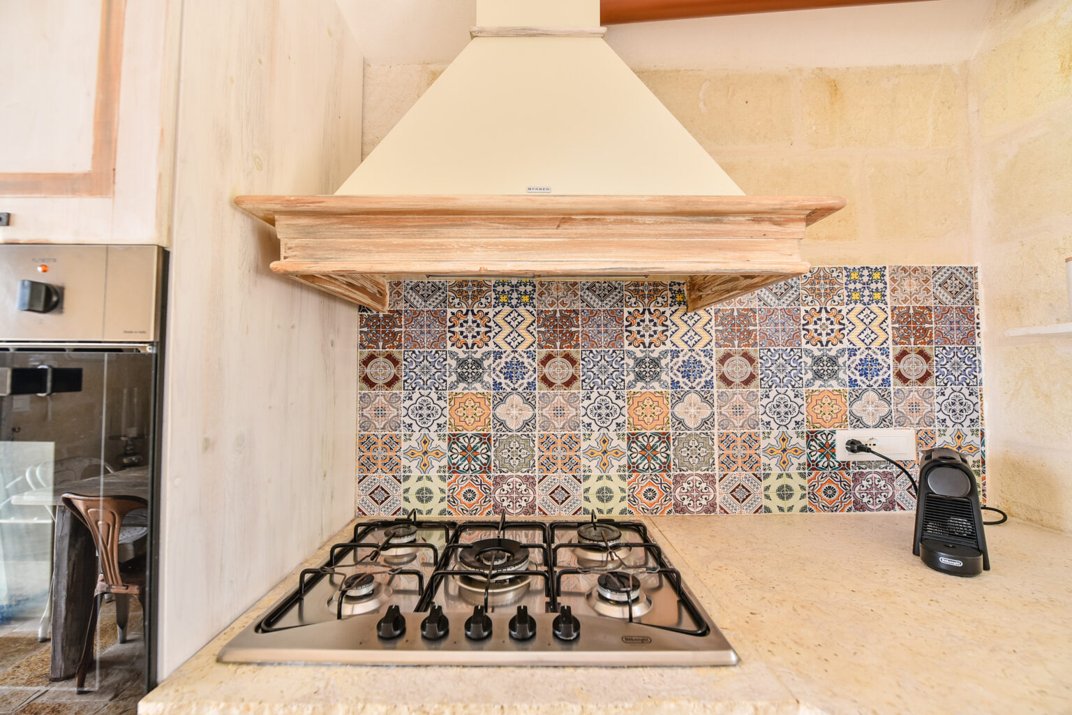 Modern kitchen with a gas stove, decorative tile backsplash featuring colorful patterns, and a wooden range hood. The design combines functionality with aesthetic appeal, ideal for contemporary cooking spaces. | Only on SopranoVillas