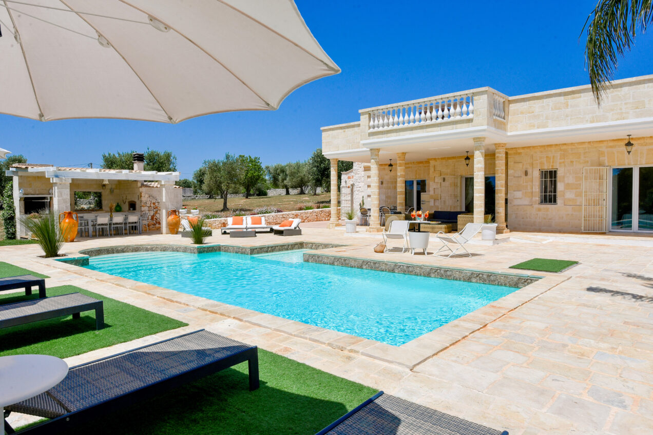 Luxury villa with a private swimming pool, sun loungers, and an outdoor dining area surrounded by olive trees under a clear blue sky. Perfect for relaxation and leisure in a tranquil setting. | Only on SopranoVillas