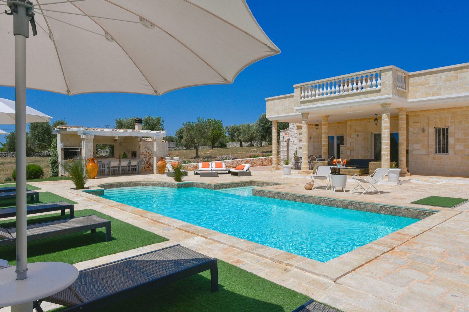 Luxury villa with a private swimming pool, sun loungers, and outdoor dining area set against a clear blue sky. Perfect for a relaxing getaway in a serene landscape. | Only on SopranoVillas
