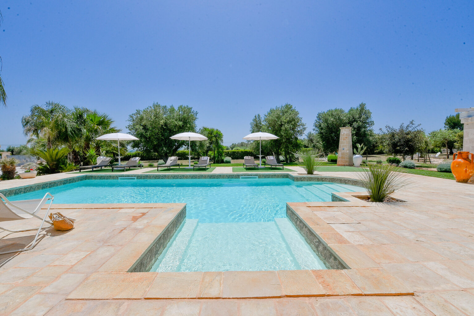 Luxurious outdoor swimming pool surrounded by lush greenery and sun loungers under white umbrellas, ideal for relaxation in a serene setting. | Only on SopranoVillas