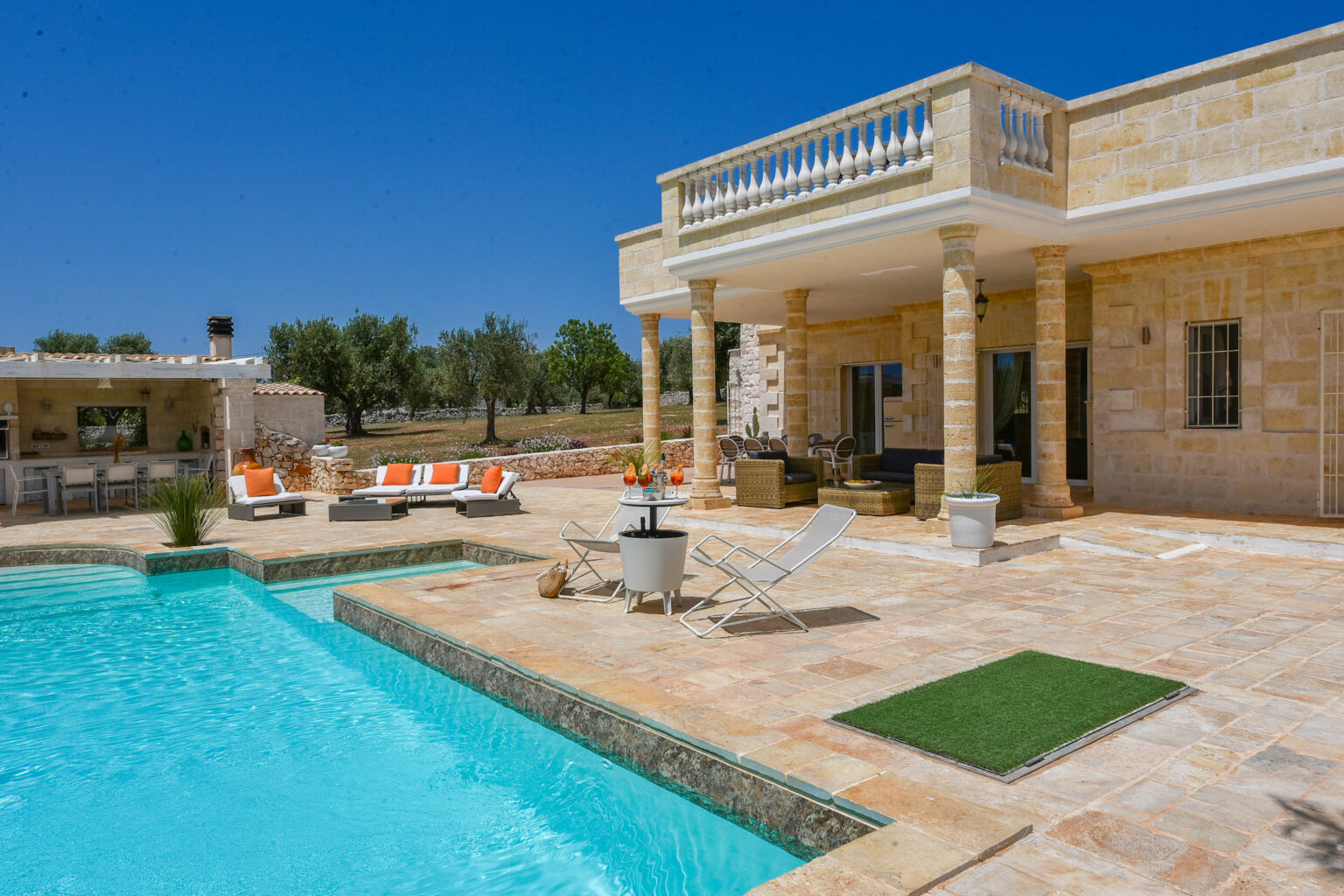 Luxury villa with a swimming pool, sun loungers, and stone architecture under a clear blue sky. Olive trees and outdoor seating area enhance the serene atmosphere. Perfect for a relaxing getaway. | Only on SopranoVillas