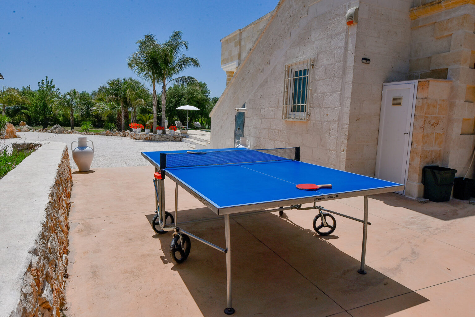 Outdoor ping pong table set up in a sunny garden area with palm trees, ideal for recreational activities. | Only on SopranoVillas