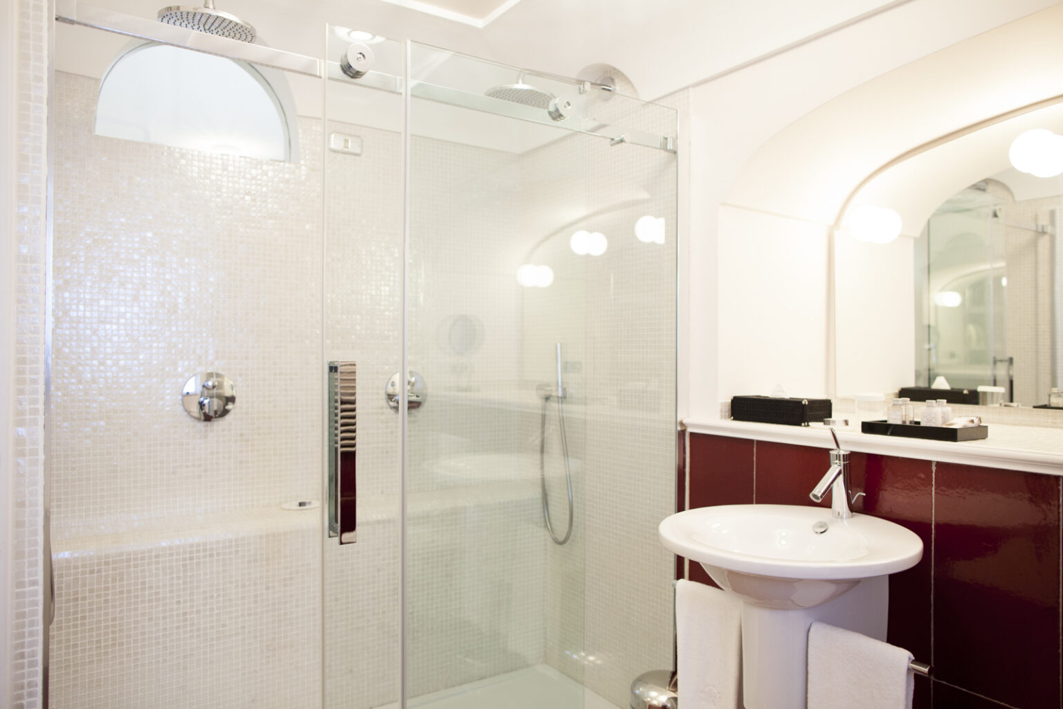 Modern bathroom featuring a glass shower enclosure, mosaic tile walls, a sleek sink with a towel rack, and elegant lighting fixtures. Ideal for showcasing contemporary design and functionality in home decor. | Only on SopranoVillas
