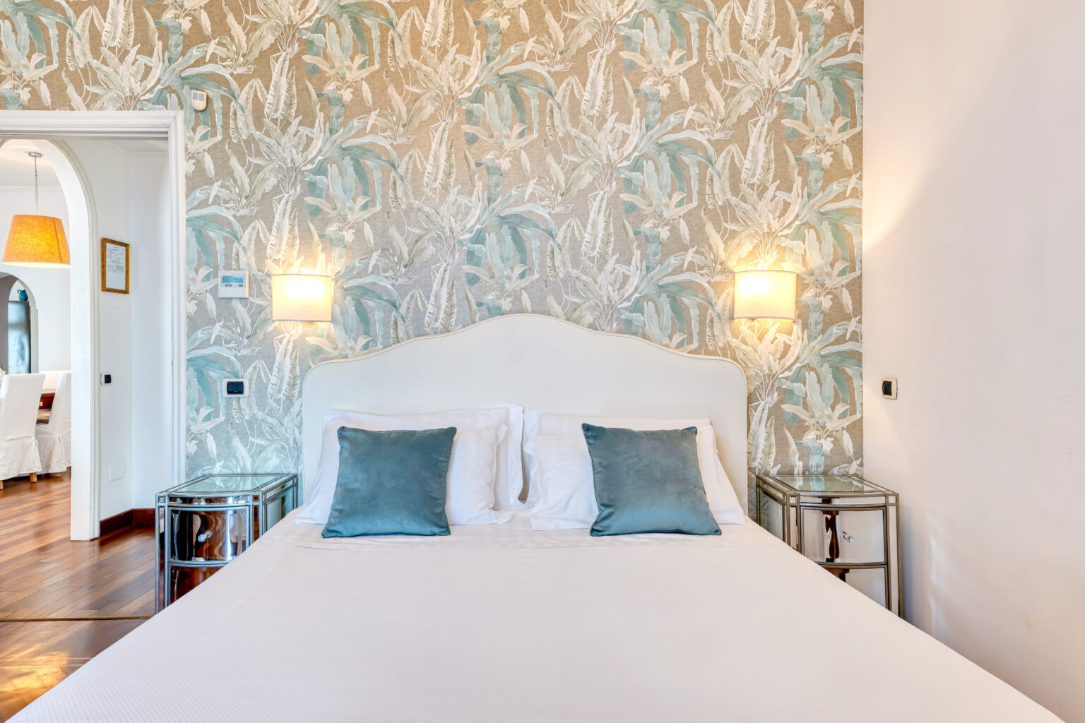Cozy bedroom featuring a plush white bed with blue accent pillows, stylish nightstands, and a decorative wallpaper with a soft pattern, creating a serene atmosphere perfect for relaxation. | Only on SopranoVillas