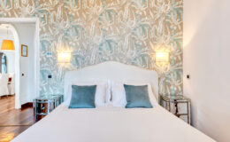 Cozy bedroom featuring a plush white bed with blue accent pillows, stylish nightstands, and a decorative wallpaper with a soft pattern, creating a serene atmosphere perfect for relaxation.