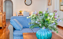 Cozy living room featuring a blue striped couch adorned with decorative pillows, a vibrant turquoise vase filled with fresh flowers, and a wooden coffee table, creating a warm and inviting atmosphere.