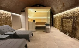 Modern spa interior featuring a sauna, comfortable lounge chairs, and natural stone walls, illuminated by soft ambient lighting. Ideal for relaxation and wellness.