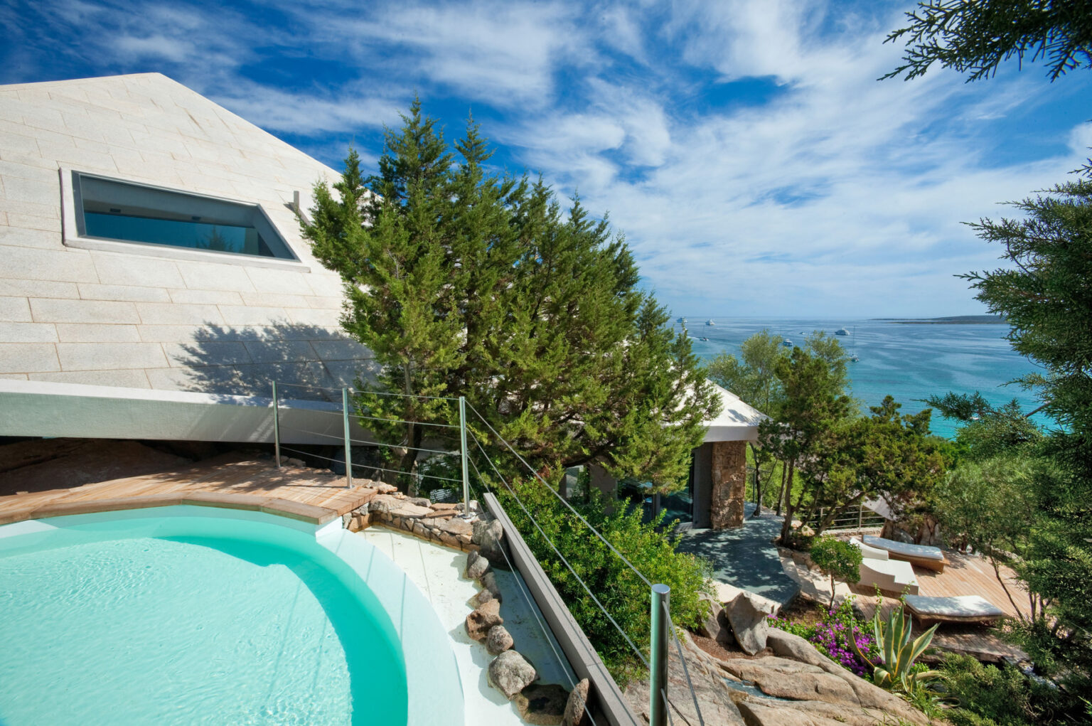 Luxury villa with a private pool overlooking the ocean, surrounded by lush greenery and tropical plants under a bright blue sky. Ideal for vacation rentals or real estate listings. | Only on SopranoVillas