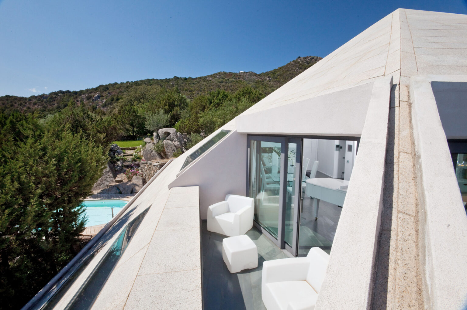 Modern architectural design of a pyramid-shaped house with a balcony overlooking a pool and lush greenery, showcasing minimalist outdoor seating and panoramic mountain views. | Only on SopranoVillas