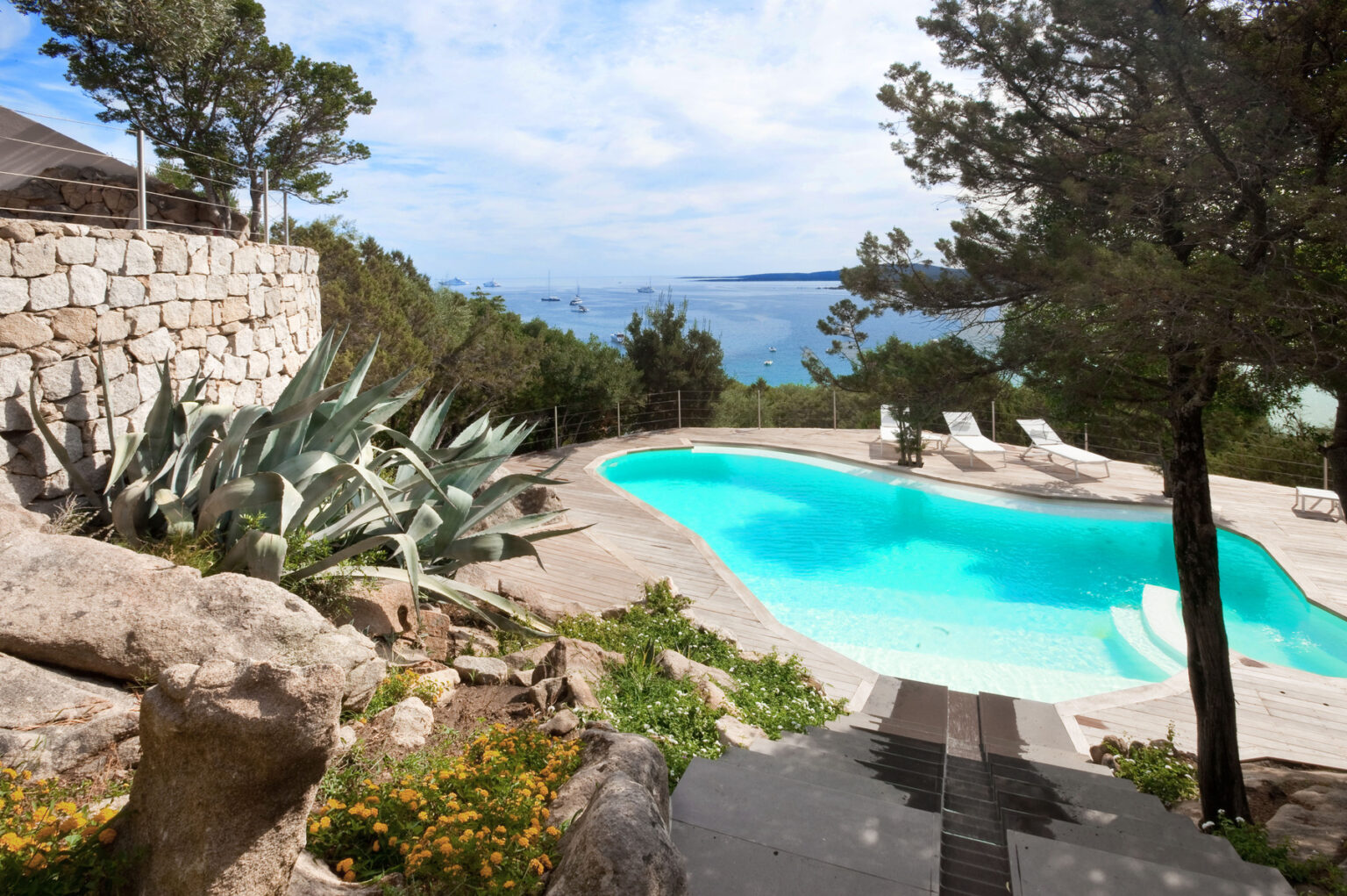 Stunning outdoor pool area with a scenic ocean view, surrounded by lush greenery and natural stone features, ideal for relaxation and leisure. | Only on SopranoVillas