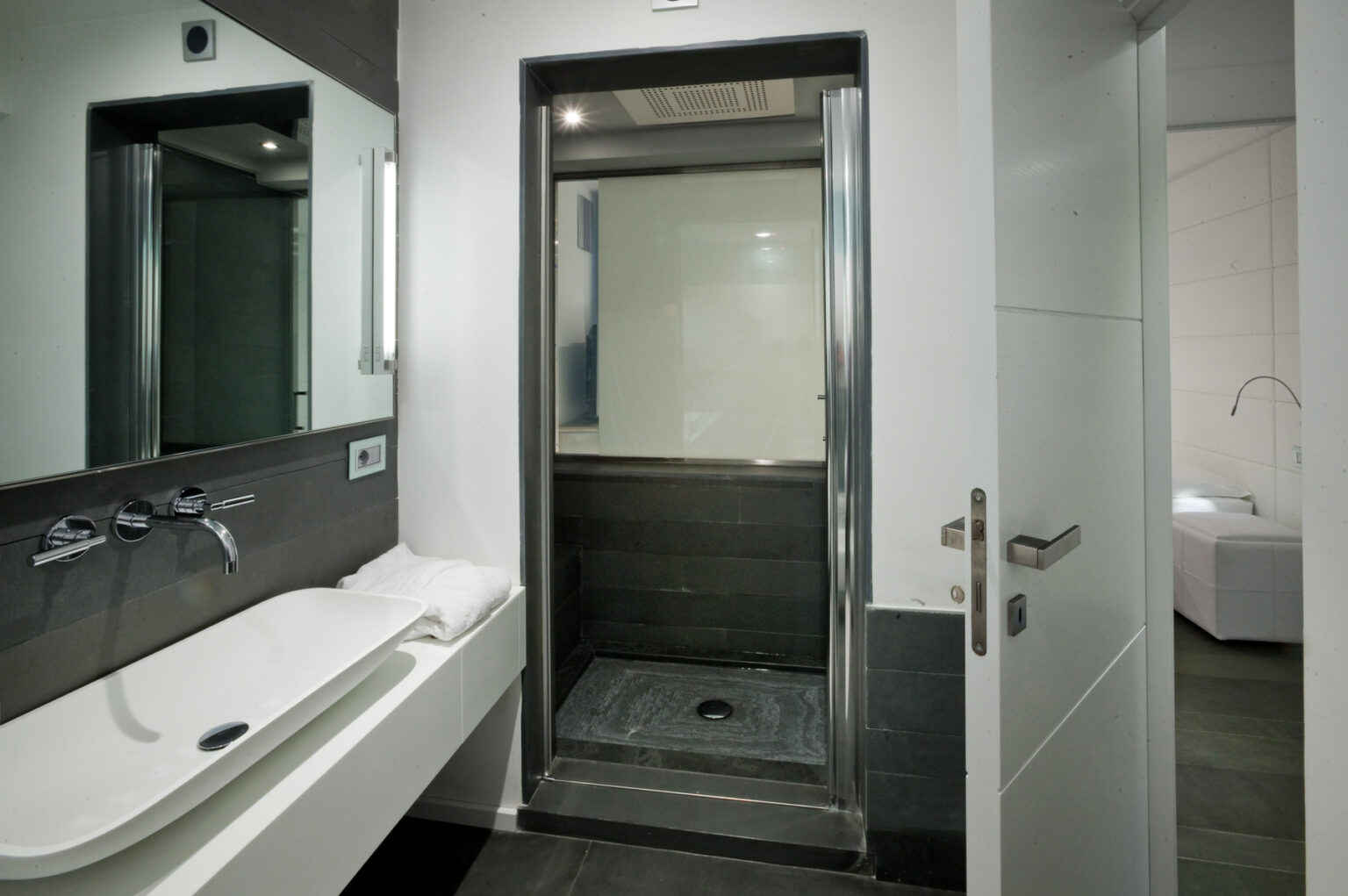 Modern bathroom featuring a sleek shower enclosure, a large mirror, and minimalist design elements. The space includes a stylish bathtub and contemporary fixtures, emphasizing a clean and sophisticated aesthetic. | Only on SopranoVillas