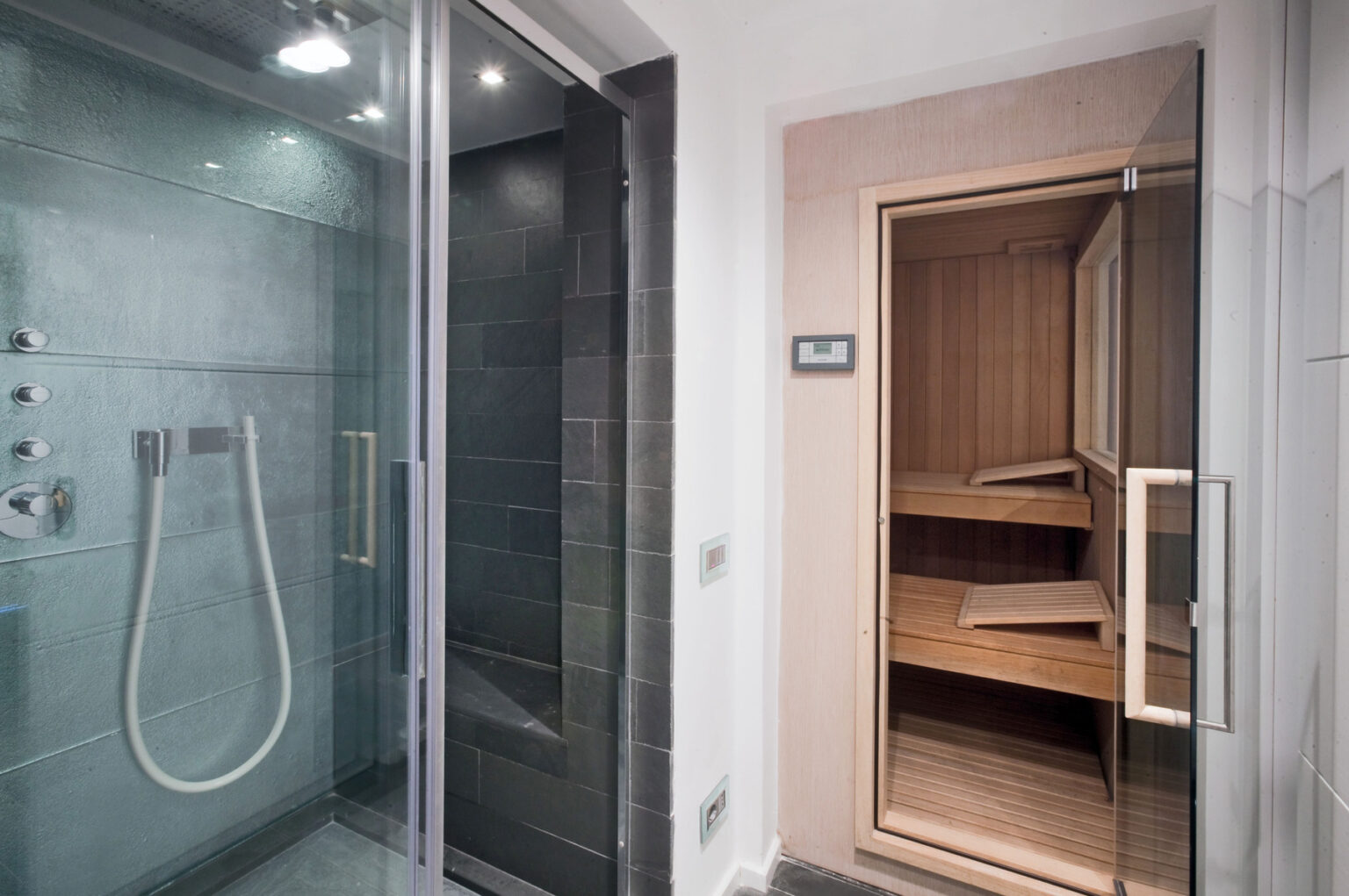 Modern bathroom featuring a glass-enclosed shower with multiple shower heads and a sleek sauna with wooden benches. The design combines luxury and functionality, ideal for relaxation and wellness. | Only on SopranoVillas