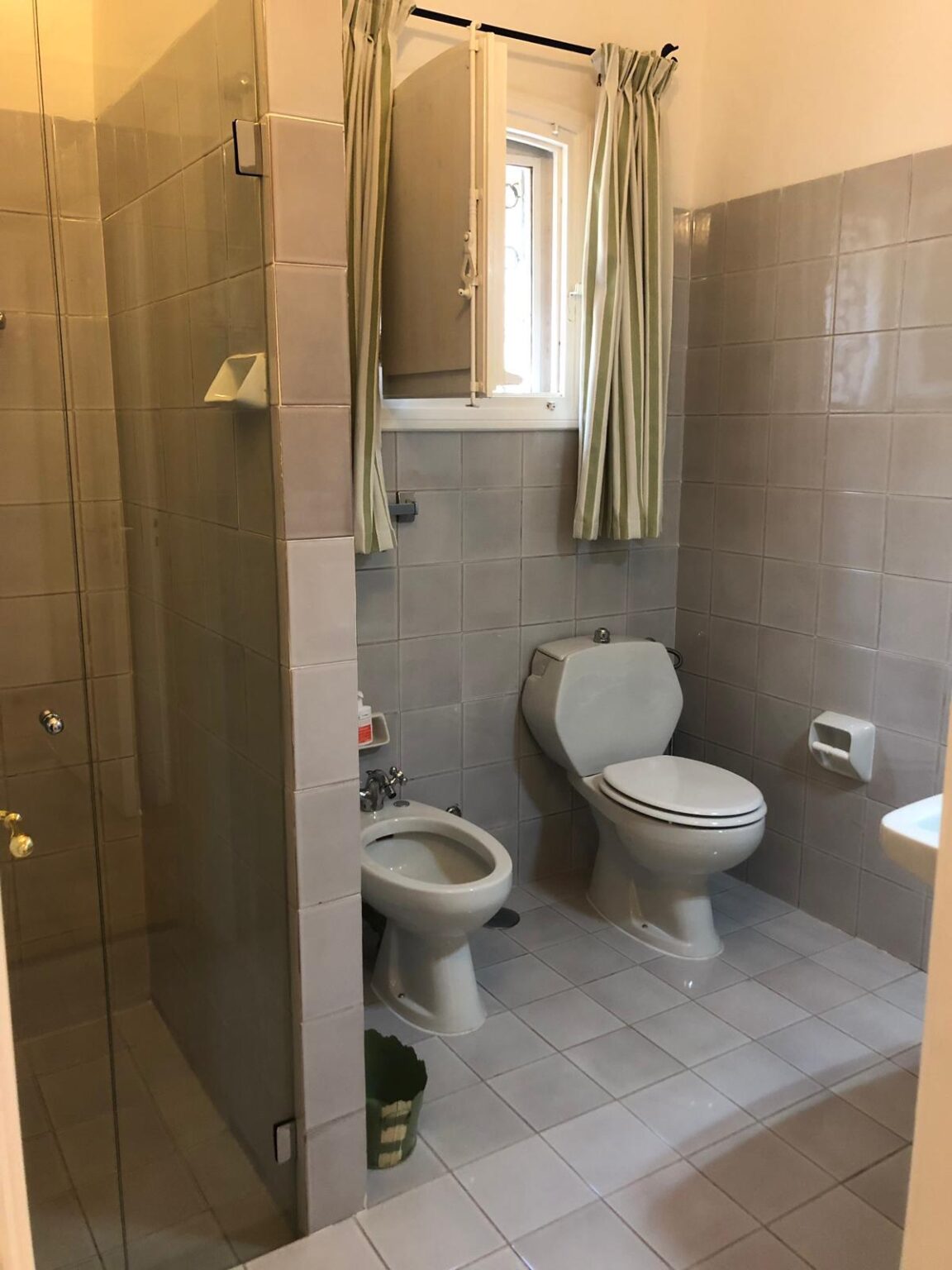 Small bathroom featuring a shower, toilet, and bidet, with light-colored tiles and window for natural light. | Only on SopranoVillas