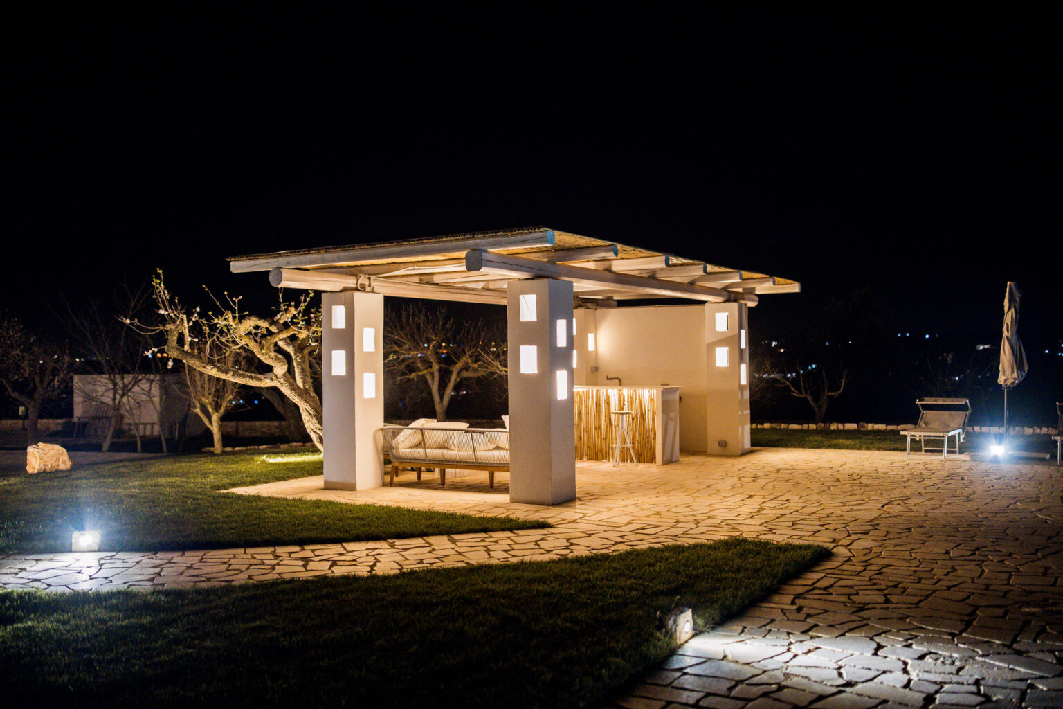Modern outdoor patio illuminated at night with stylish lighting, featuring a comfortable seating area and landscaped surroundings. | Only on SopranoVillas