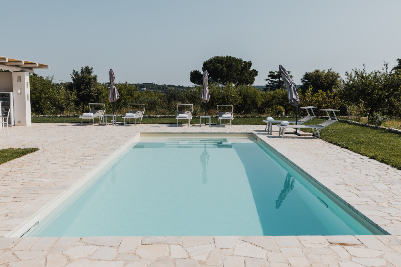 Modern outdoor swimming pool surrounded by lounge chairs and a landscaped garden, perfect for relaxation and leisure. | Only on SopranoVillas