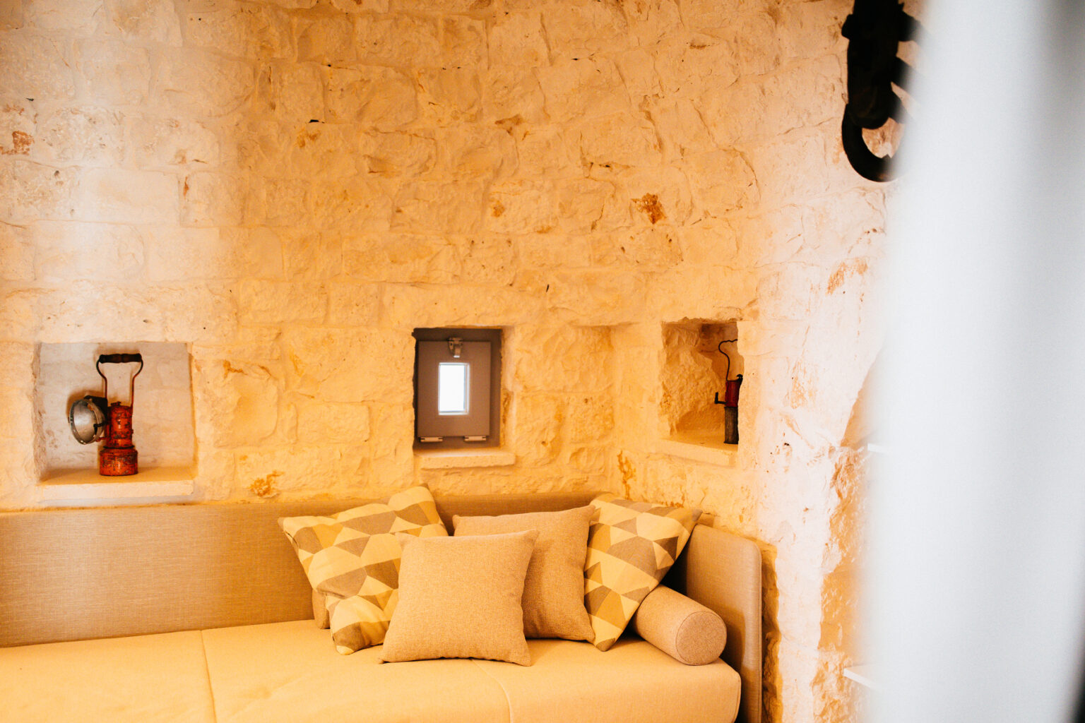 Cozy interior of a stone-walled room featuring a comfortable couch with decorative pillows, small windows, and rustic decor elements. Ideal for showcasing a warm and inviting atmosphere. | Only on SopranoVillas