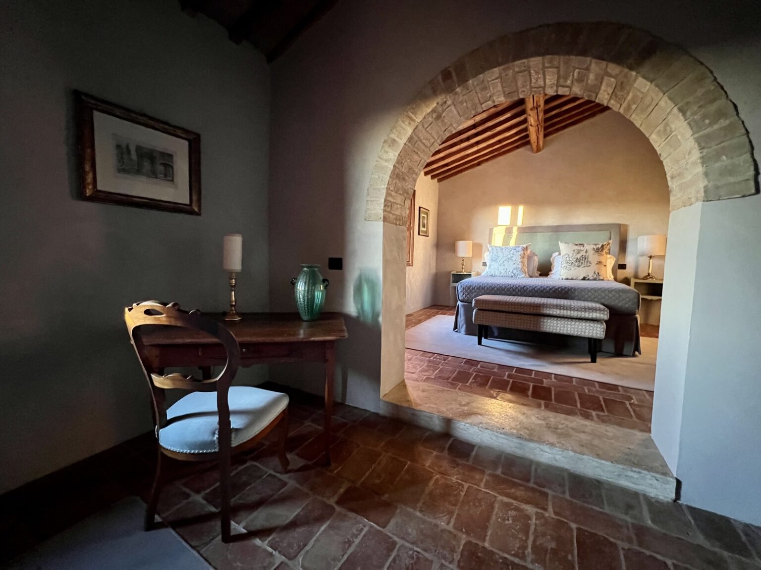 Cozy bedroom with an arched entrance, featuring a comfortable bed and elegant decor. A wooden desk with a lamp and decorative vases adds a touch of sophistication to the inviting space. | Only on SopranoVillas