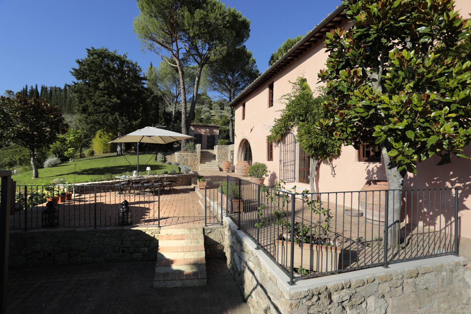 Charming rustic villa surrounded by lush greenery, featuring a spacious patio with outdoor seating under an umbrella, and a picturesque garden in a serene landscape. Ideal for relaxation and outdoor gatherings. | Only on SopranoVillas