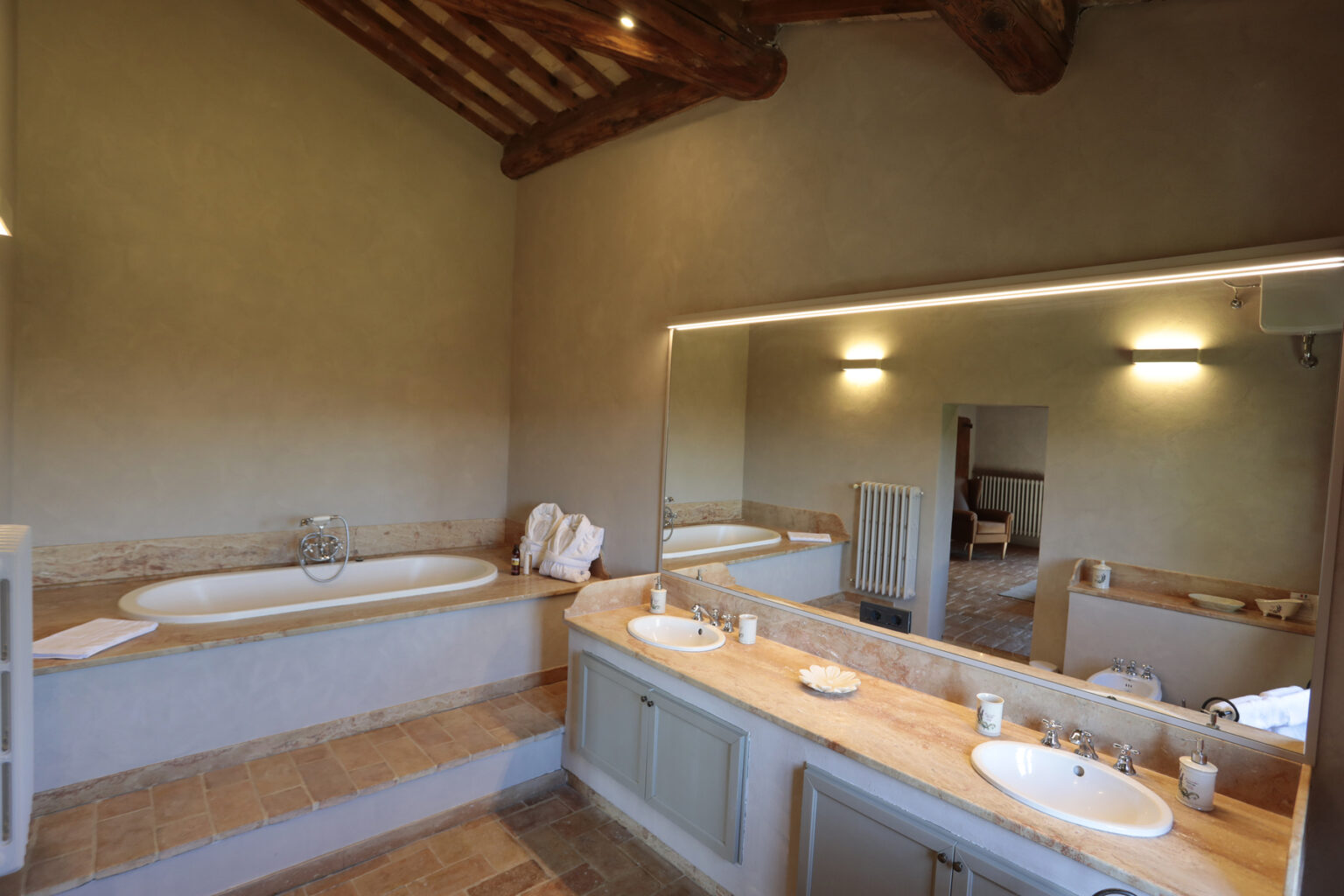 Spacious bathroom featuring a bathtub, dual sinks with elegant fixtures, and a large mirror, complemented by rustic wooden beams and a neutral color palette. Ideal for relaxation and comfort. | Only on SopranoVillas