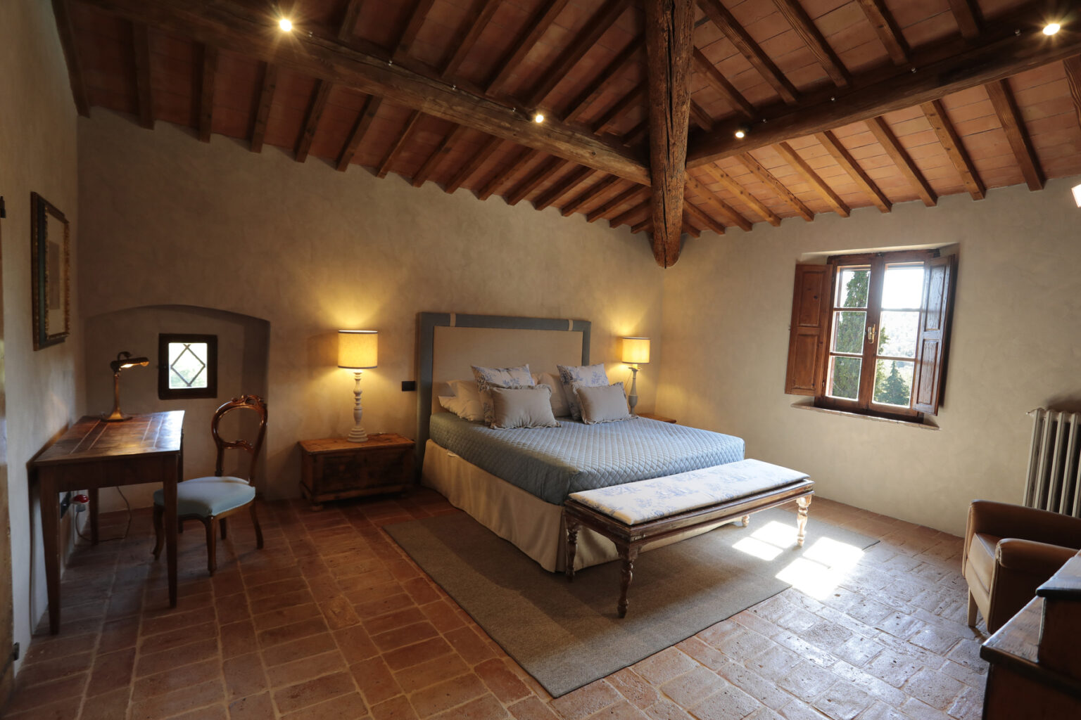 Cozy bedroom with wooden beams, featuring a comfortable bed, a small desk with a chair, and natural light from a window, creating a warm and inviting atmosphere. | Only on SopranoVillas