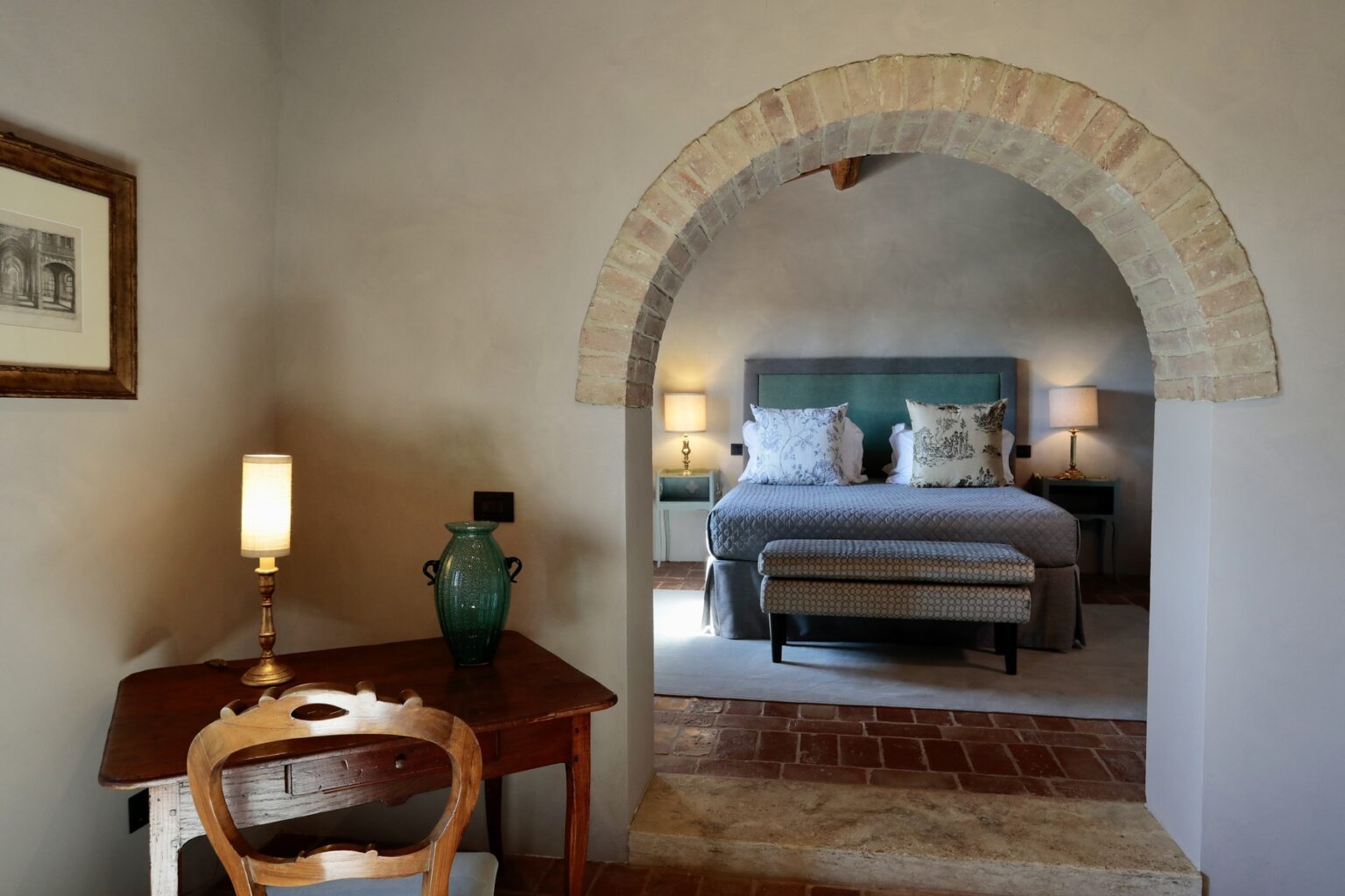Cozy bedroom interior with an arched doorway, featuring a comfortable bed, bedside lamps, and a wooden desk with a decorative vase, creating a warm and inviting atmosphere. | Only on SopranoVillas