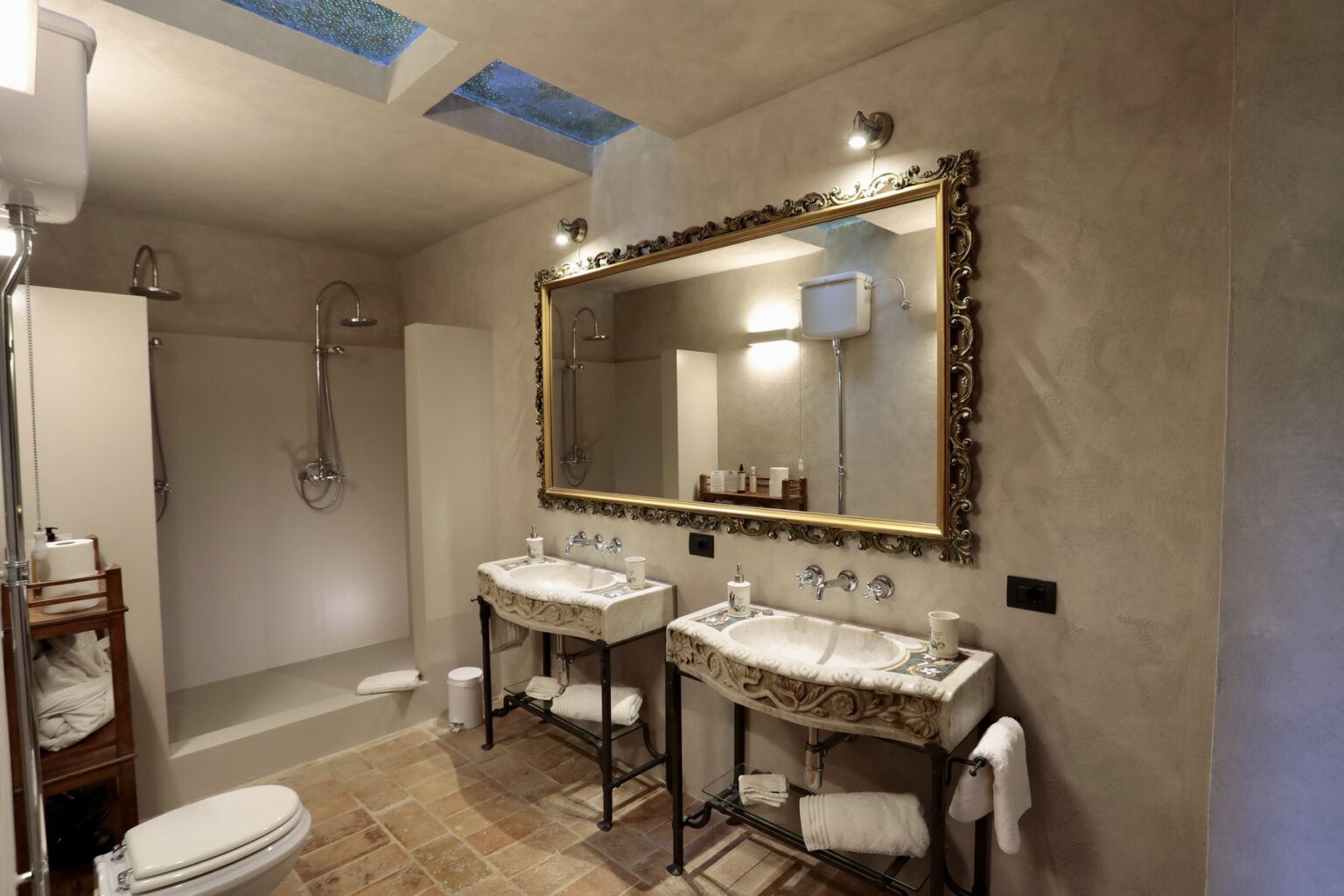 Elegant bathroom featuring dual vanities with ornate mirrors, a spacious shower area, and natural light from skylights, showcasing a modern and luxurious design. | Only on SopranoVillas