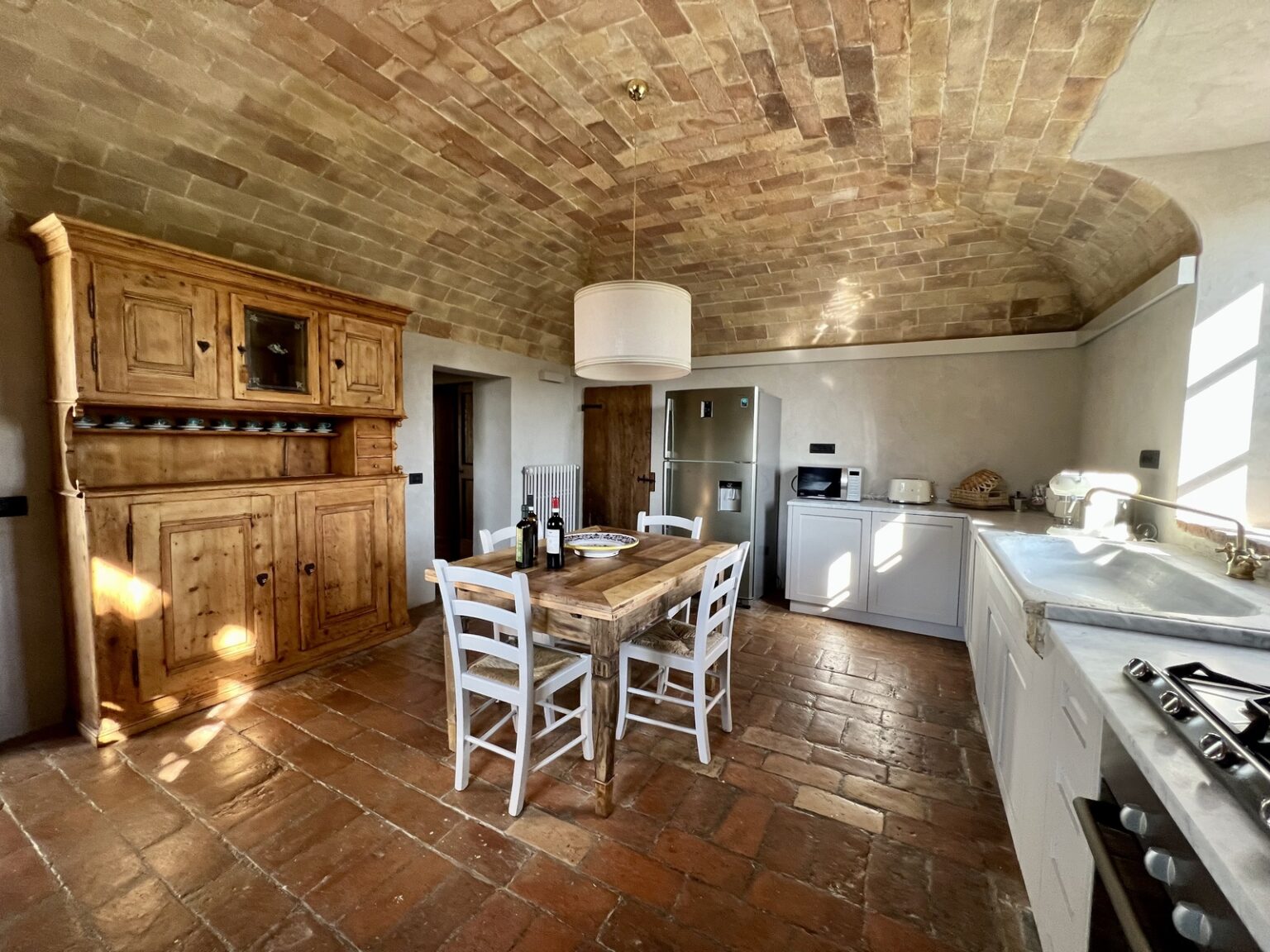 Spacious rustic kitchen with vaulted brick ceiling, wooden dining table and chairs, modern appliances, and natural light illuminating the room. | Only on SopranoVillas
