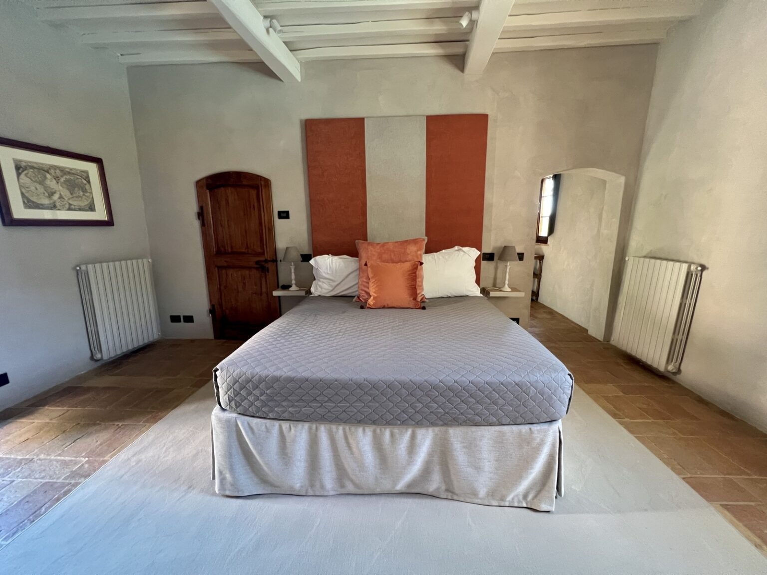 Cozy bedroom featuring a queen-sized bed with gray bedding and an orange accent pillow, warm wooden accents, and minimalist decor, creating a serene atmosphere. | Only on SopranoVillas