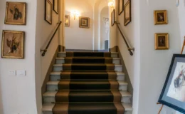 Elegant staircase leading to an arched hallway, featuring a patterned runner, framed artwork on the walls, and soft lighting enhancing the ambiance.