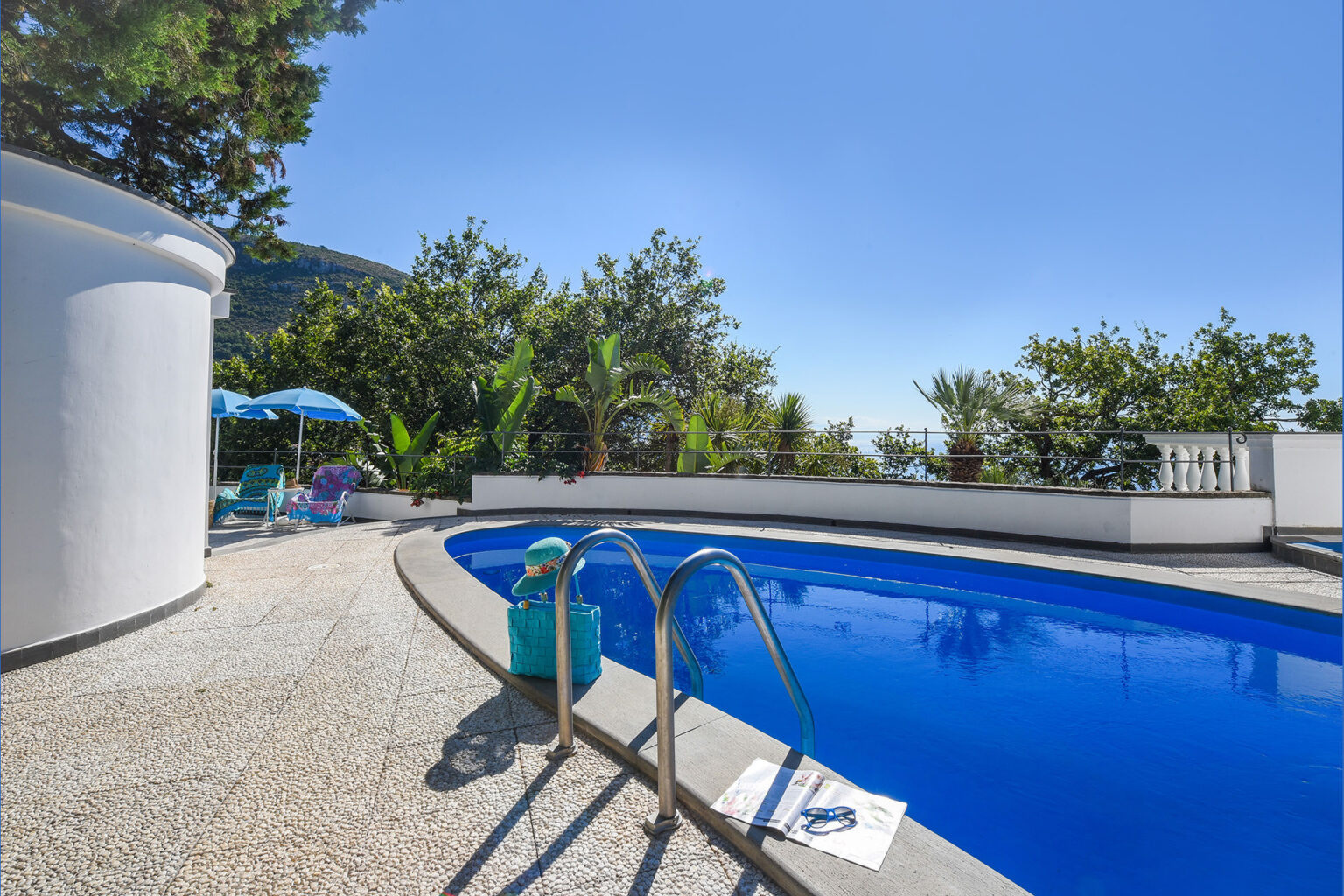 Luxury outdoor pool surrounded by lush greenery and sun loungers, with clear blue skies and a serene atmosphere, perfect for relaxation and leisure. | Only on SopranoVillas