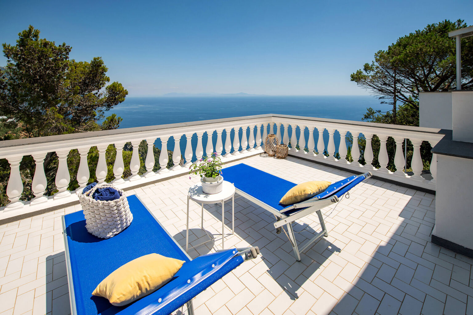 Sun loungers on a terrace overlooking the ocean, surrounded by greenery and a white railing, perfect for relaxation and enjoying scenic views. | Only on SopranoVillas