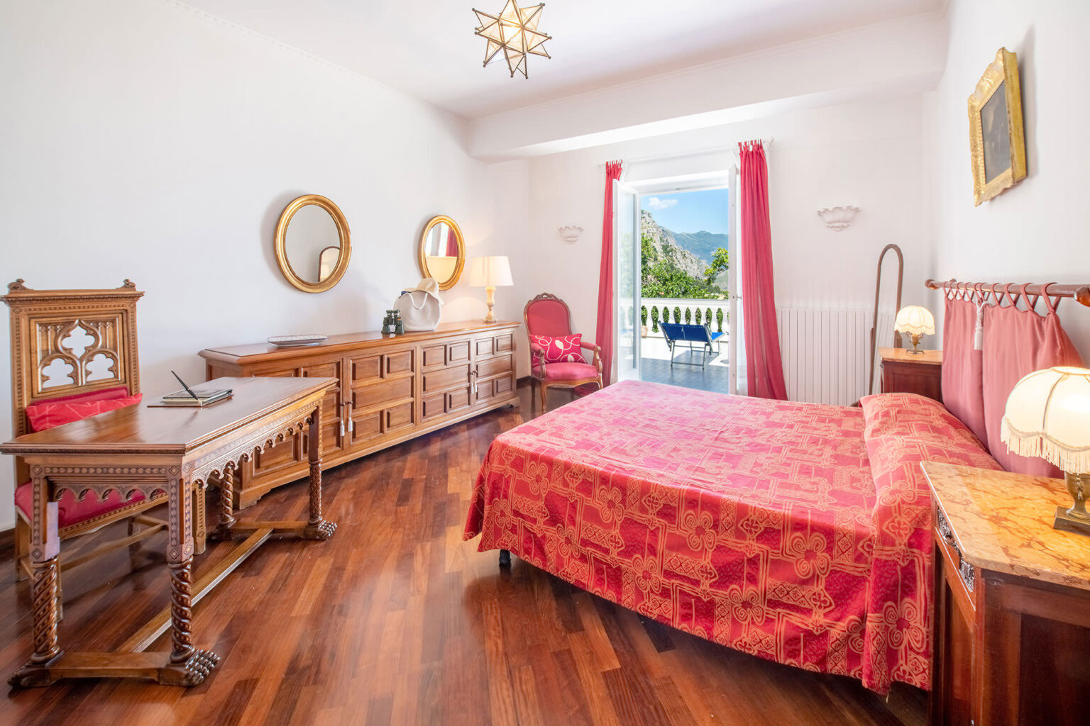 Spacious bedroom with a red floral bedspread, wooden furniture, and large windows offering natural light and scenic views. Ideal for a cozy and elegant atmosphere. | Only on SopranoVillas