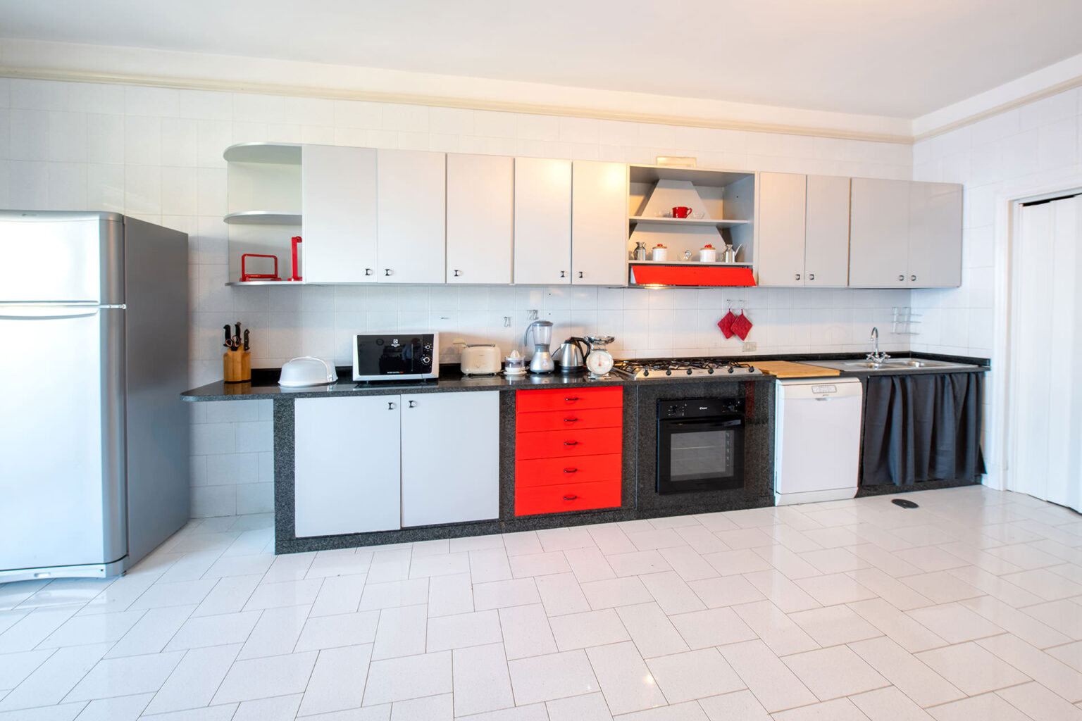 Modern kitchen with sleek gray and white cabinetry, featuring red accents, stainless steel appliances, and a spacious layout. Ideal for cooking and entertaining. | Only on SopranoVillas