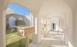 Bright and airy corridor with arched windows, featuring stone planters and views of a landscaped garden, showcasing modern architectural design and natural light.