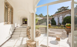 Bright and airy interior view of a modern hallway leading to a landscaped garden, featuring large glass doors, white tiled floors, and decorative stone elements.