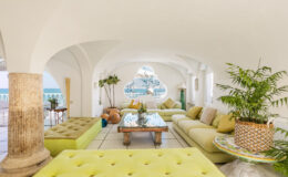 Bright and airy lounge area featuring modern green seating, decorative plants, and a stunning ocean view through an arched window, perfect for relaxation and social gatherings.