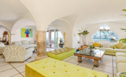 Spacious and bright living room featuring arched ceilings, modern furniture, and colorful decor, with large windows offering scenic views and natural light.