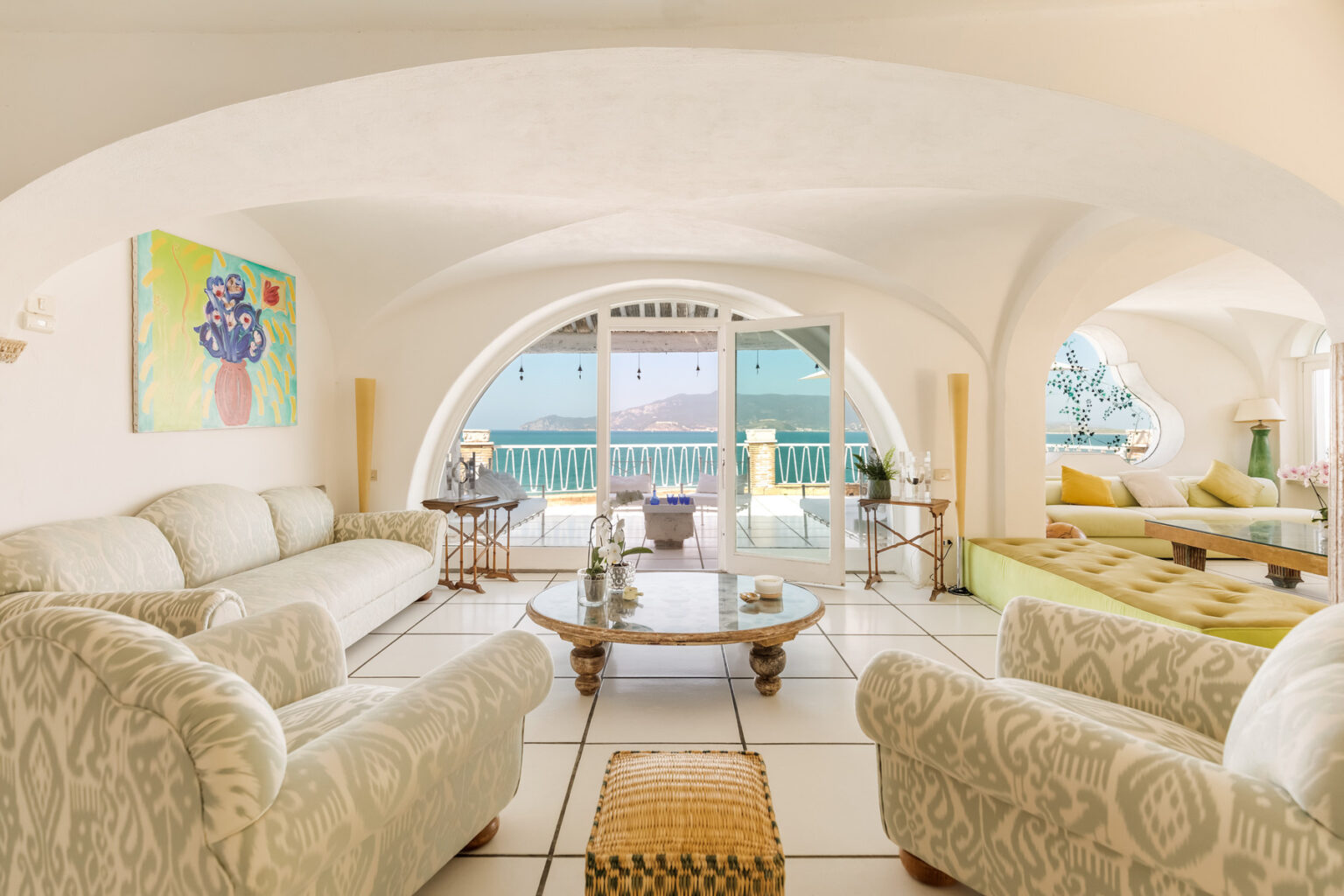 Spacious and elegantly designed living room featuring a light color palette, plush sofas, and natural light streaming through large arched windows. The room is adorned with contemporary art and tasteful décor, creating a warm and inviting atmosphere. | Only on SopranoVillas