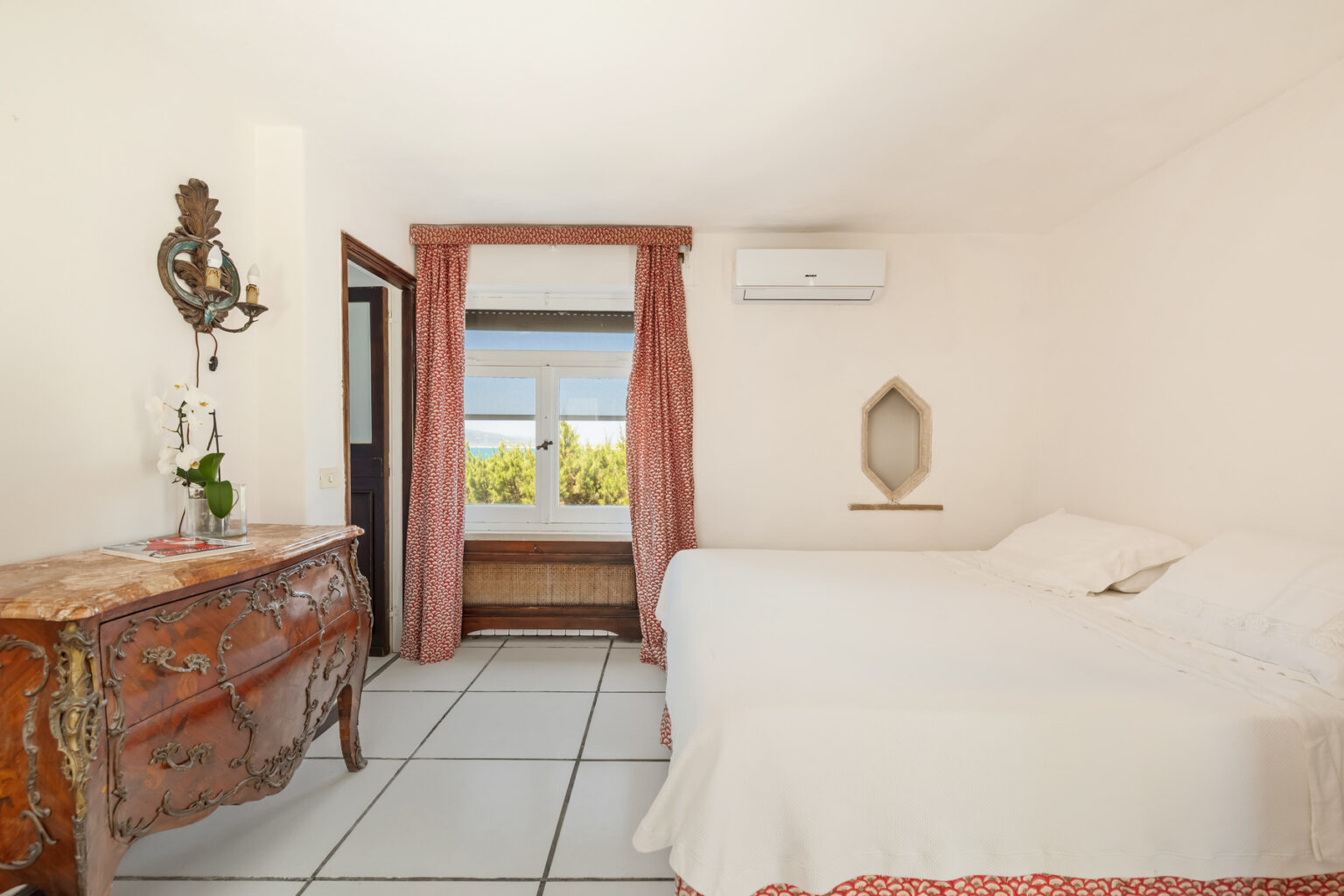 Cozy bedroom featuring a white bed, vintage dresser, and large window with scenic views, complemented by soft curtains and air conditioning for comfort. | Only on SopranoVillas