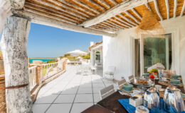 Outdoor dining area with a wooden pergola overlooking a seaside view, featuring a table set with elegant tableware and a relaxing atmosphere, ideal for enjoying meals in a coastal setting.