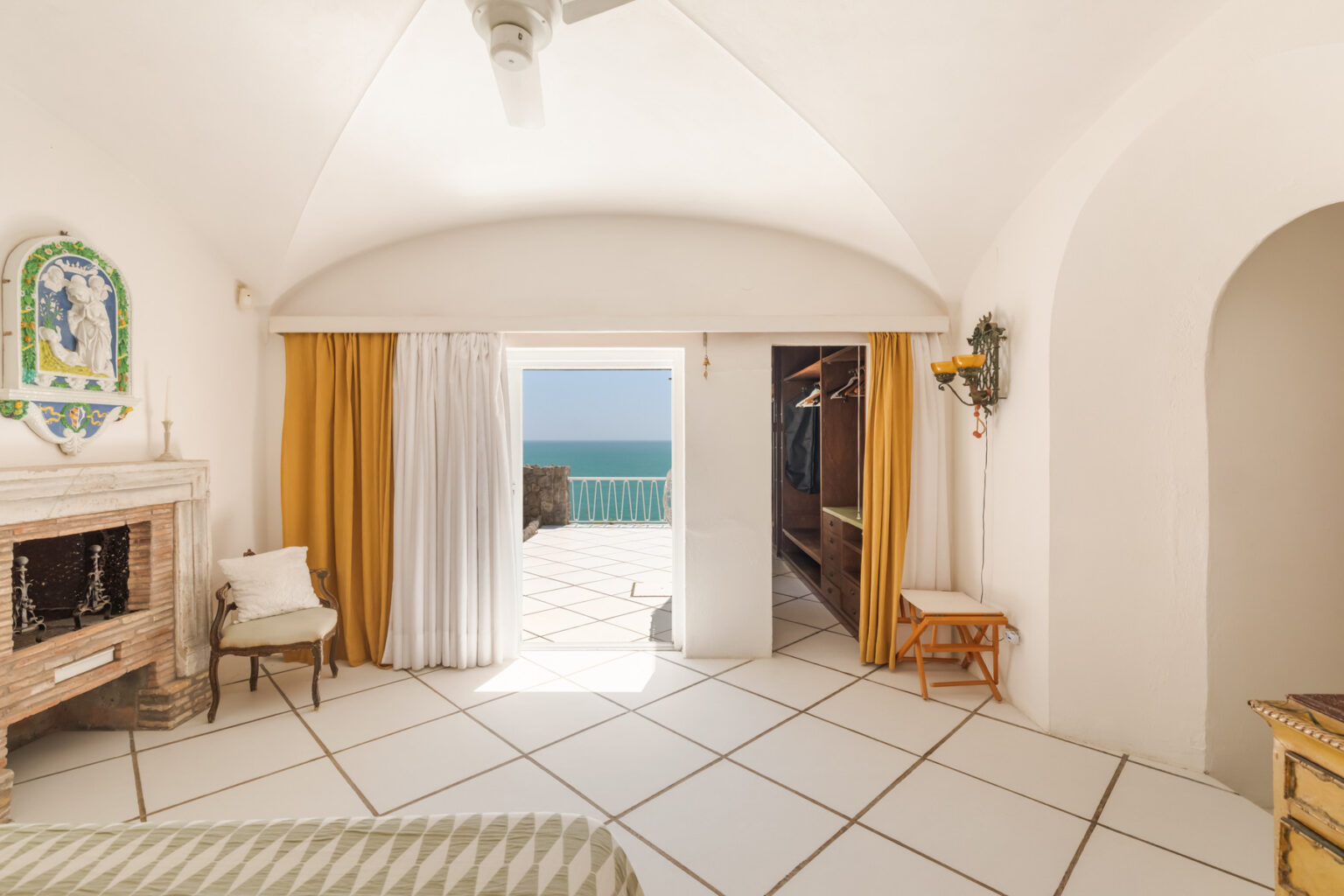 Bright and airy hotel room with white walls and tiled floor, featuring large windows with ocean views, elegant furnishings, and stylish decor. Perfect for a coastal getaway. | Only on SopranoVillas